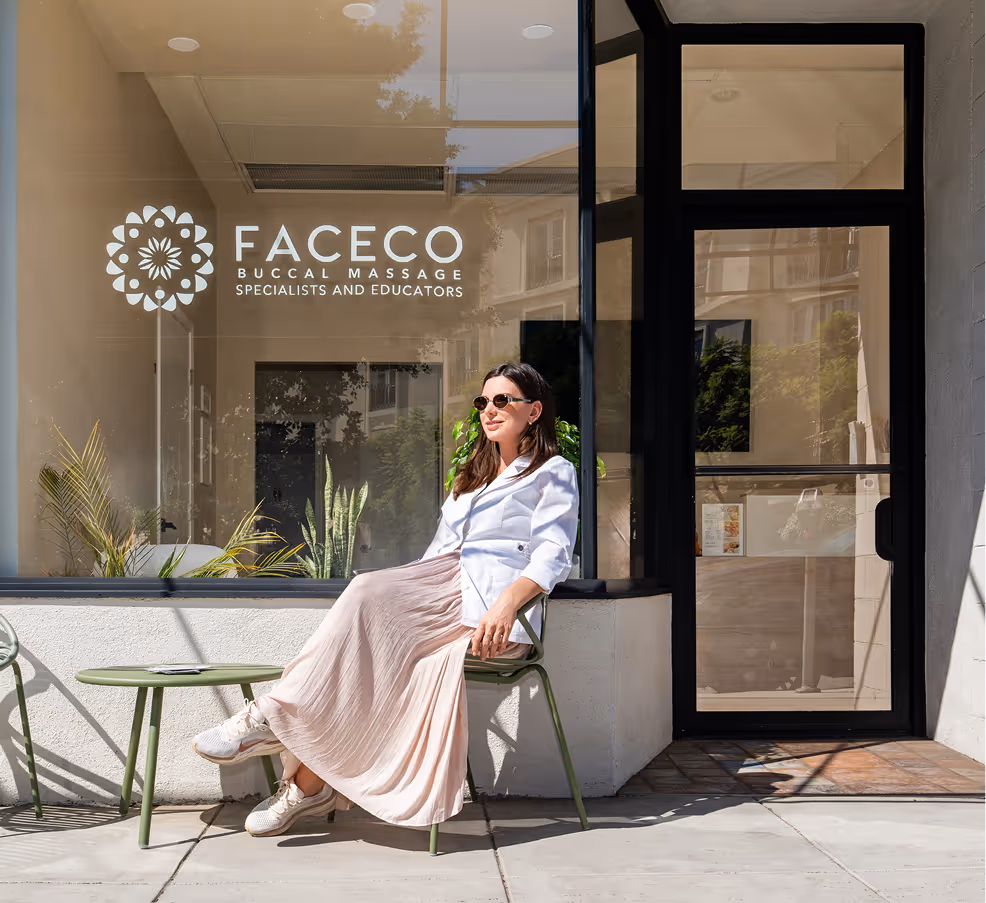 Polina sitting outside FACECO Buccal Massage specialists and educators clinic on a green chair.