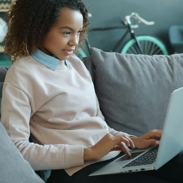 Woman using a laptop while sitting on a couch.