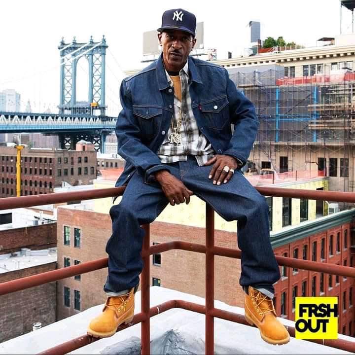 Rakim sitting on a rooftop with New York City in the background