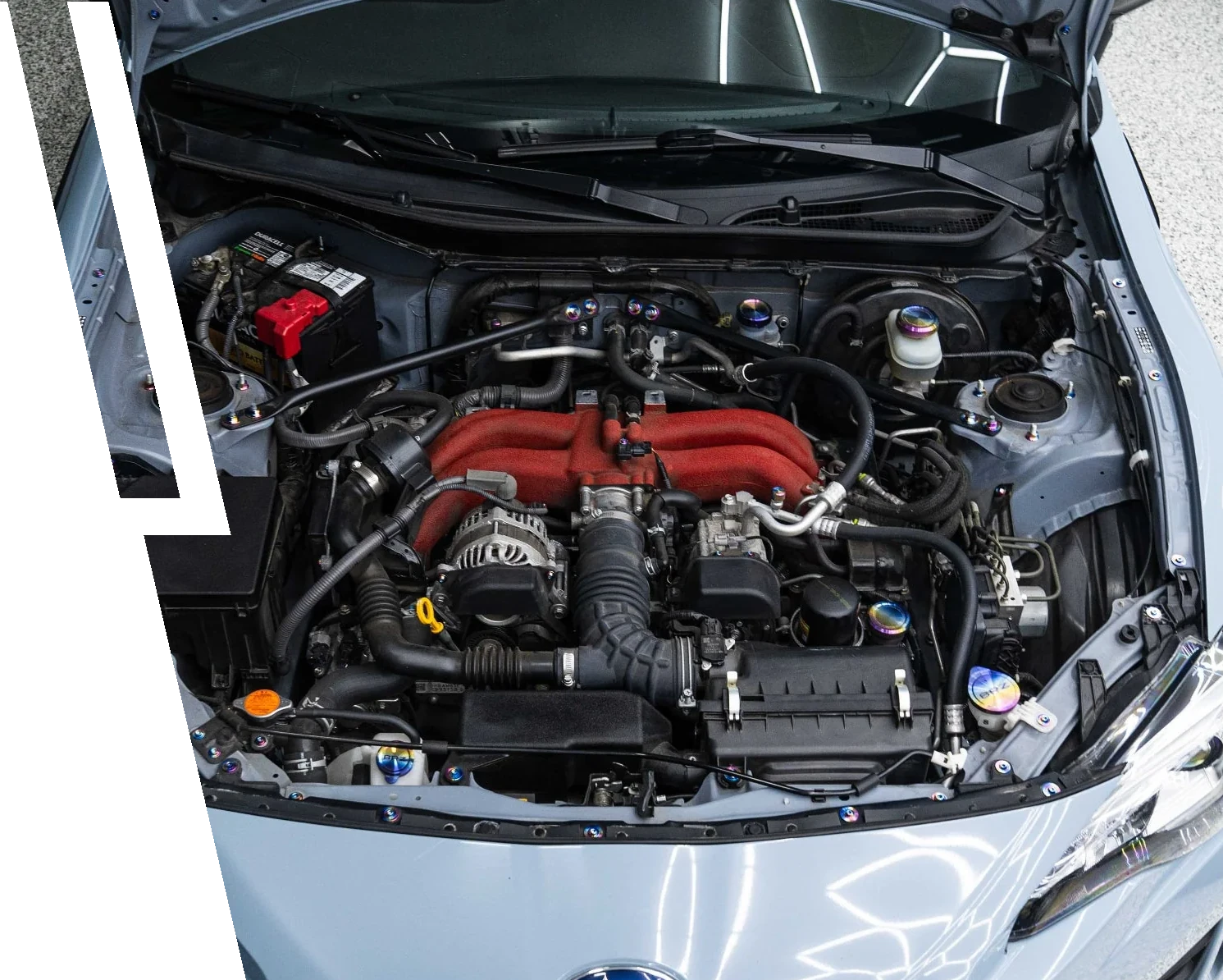Open car hood showing a clean engine bay with red intake manifold and various black hoses and components.