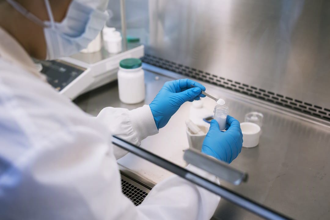Gloved hands compounding medication in pharmacy lab