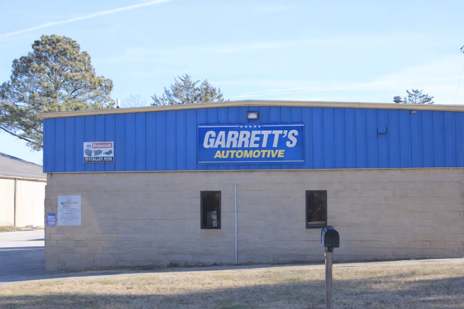 Blue and beige building with a large sign reading 'Garrett's Automotive' and smaller signs for Motorcraft and inspection station.