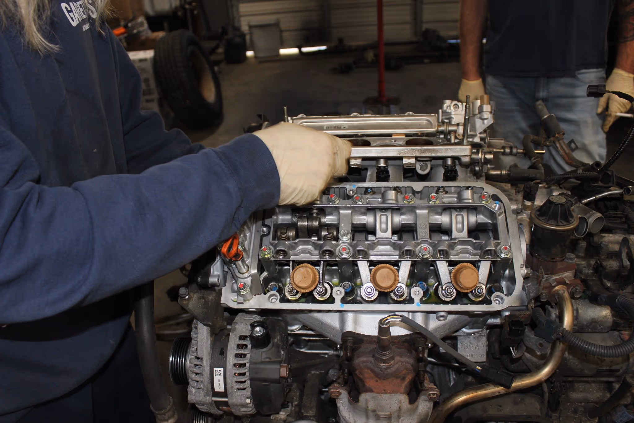 Person wearing gloves working on the internal components of a car engine inside a garage.