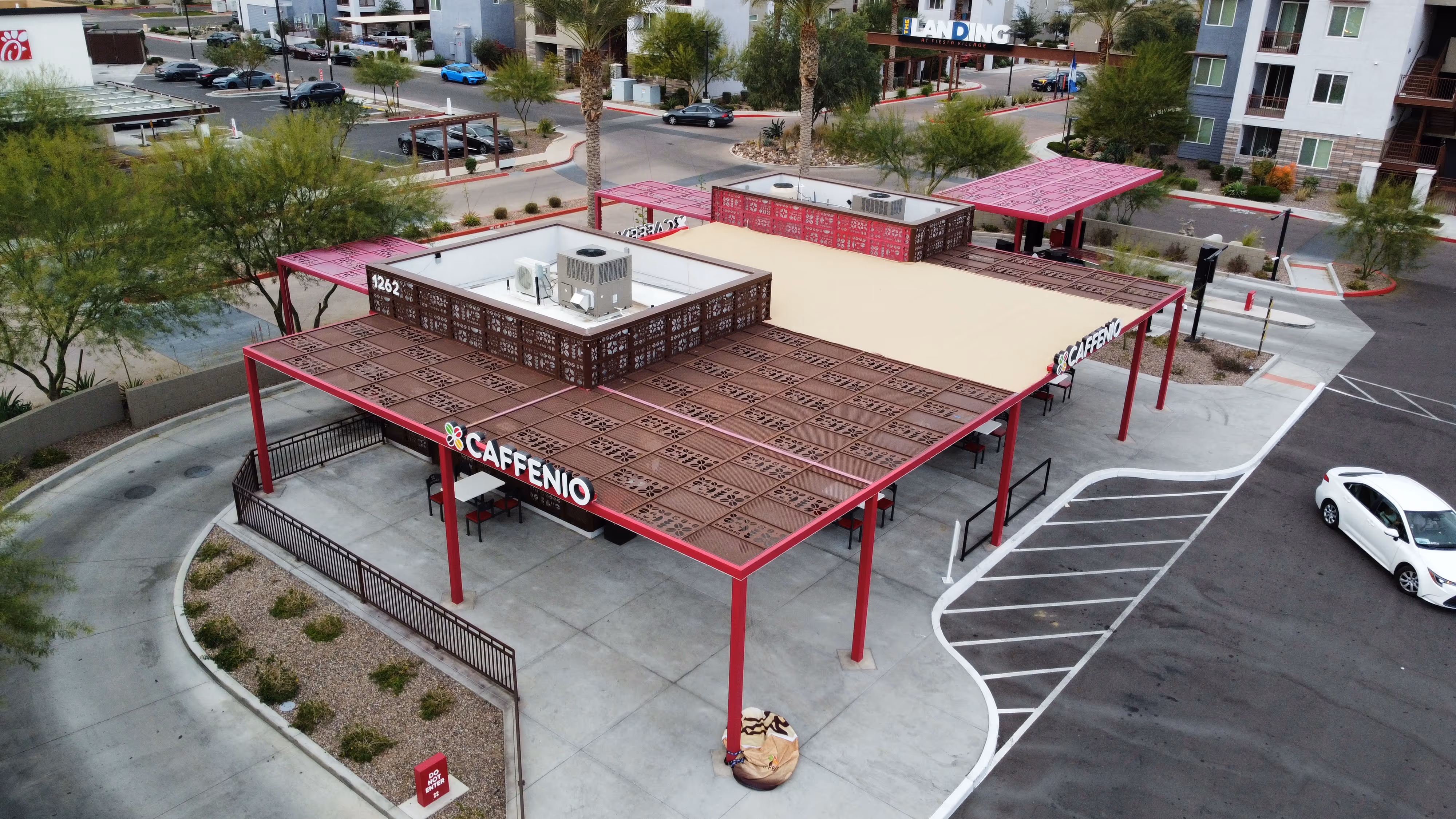 Aerial view of Caffenio coffee shop with outdoor seating and decorative roof panels in a suburban area.