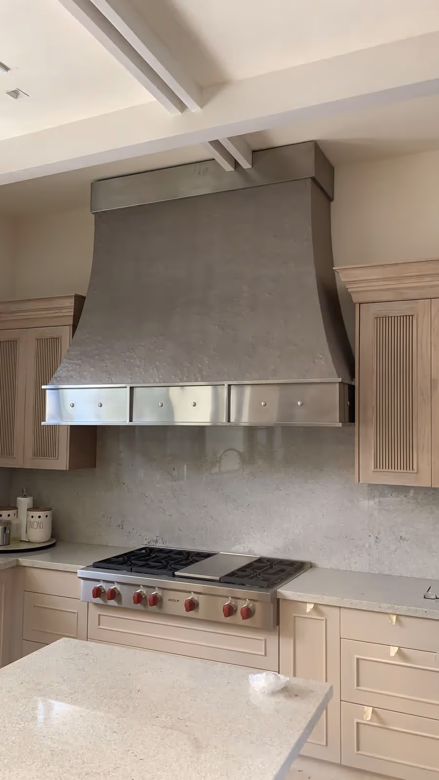Modern kitchen with stainless steel range hood above a stove with red knobs and beige cabinetry.