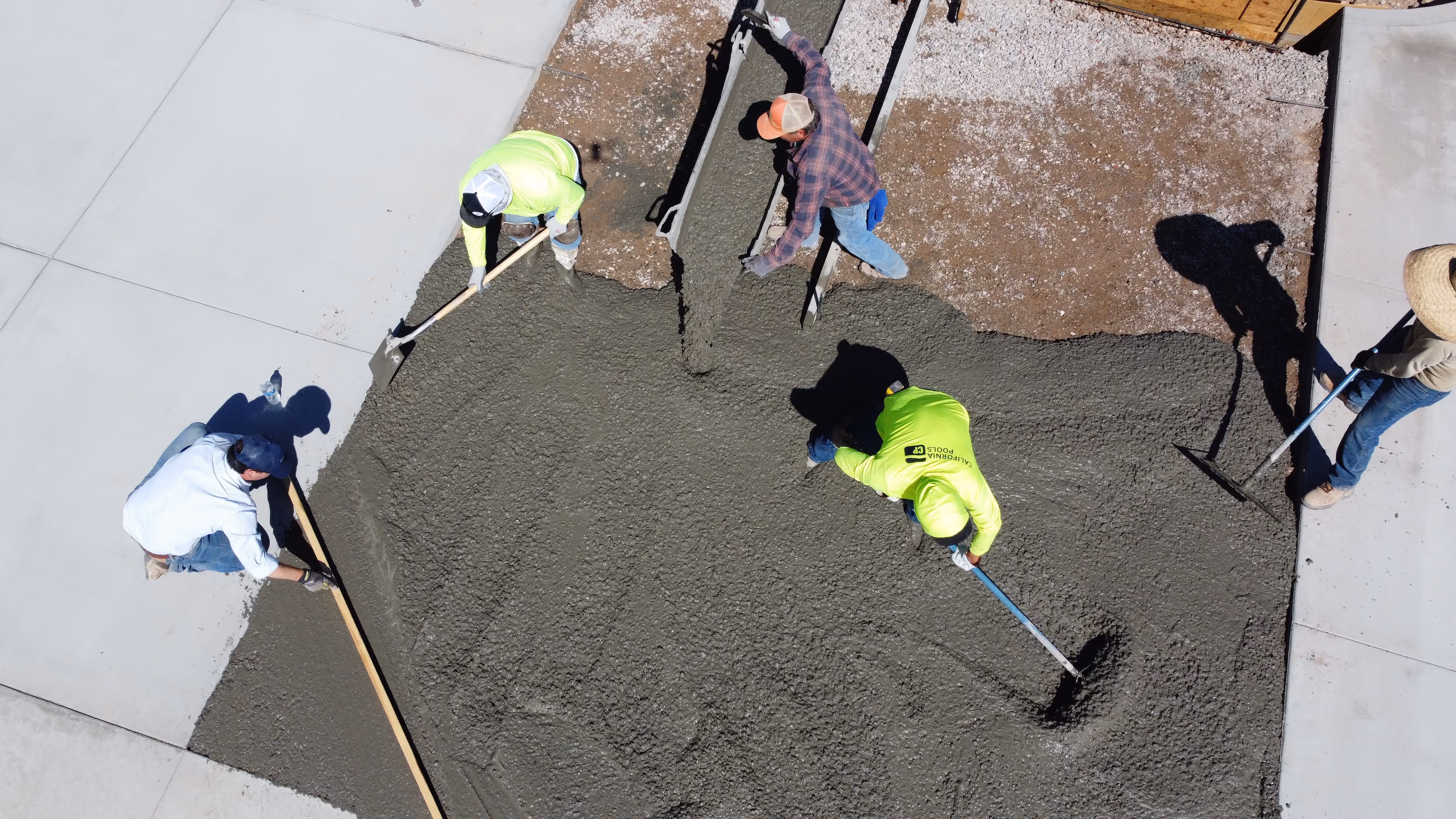 Aerial view of five workers spreading and leveling wet concrete on a construction site.