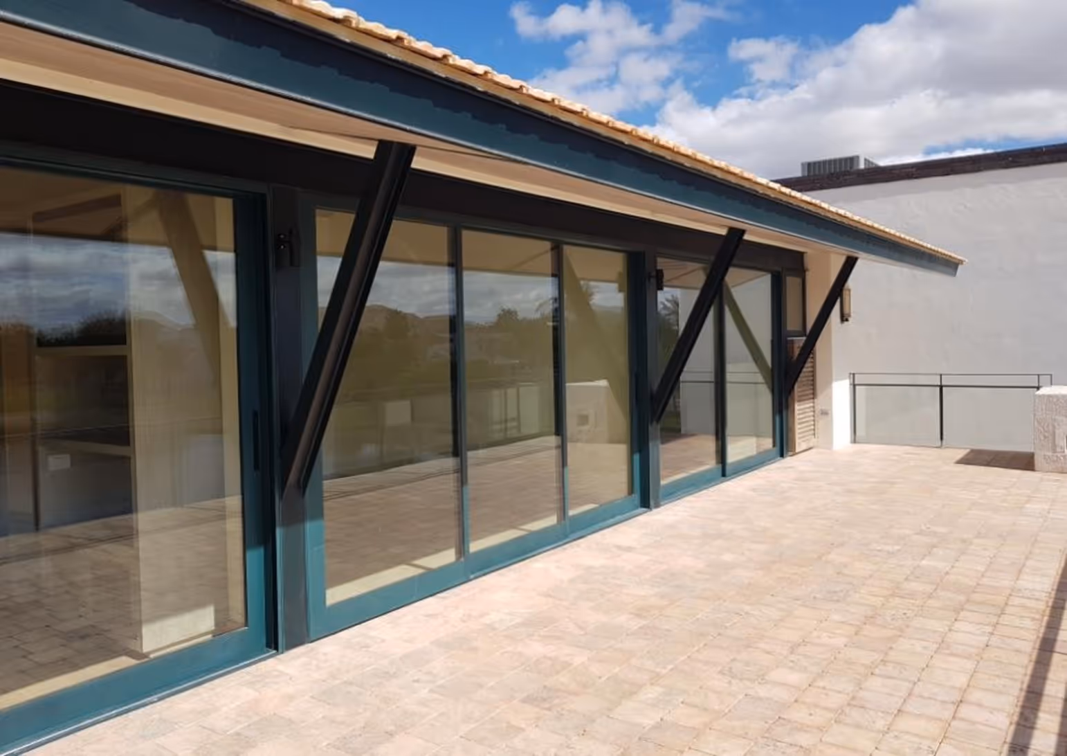 Spacious outdoor terrace with beige tiled floor and large glass sliding doors under a tiled roof.