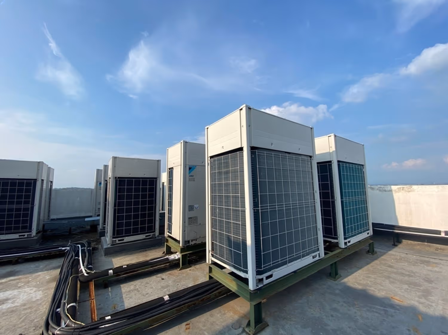 Multiple rooftop HVAC units installed on a concrete surface under a blue sky with scattered clouds.