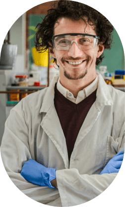 Smiling male scientist wearing safety goggles, lab coat, and blue gloves in a laboratory.
