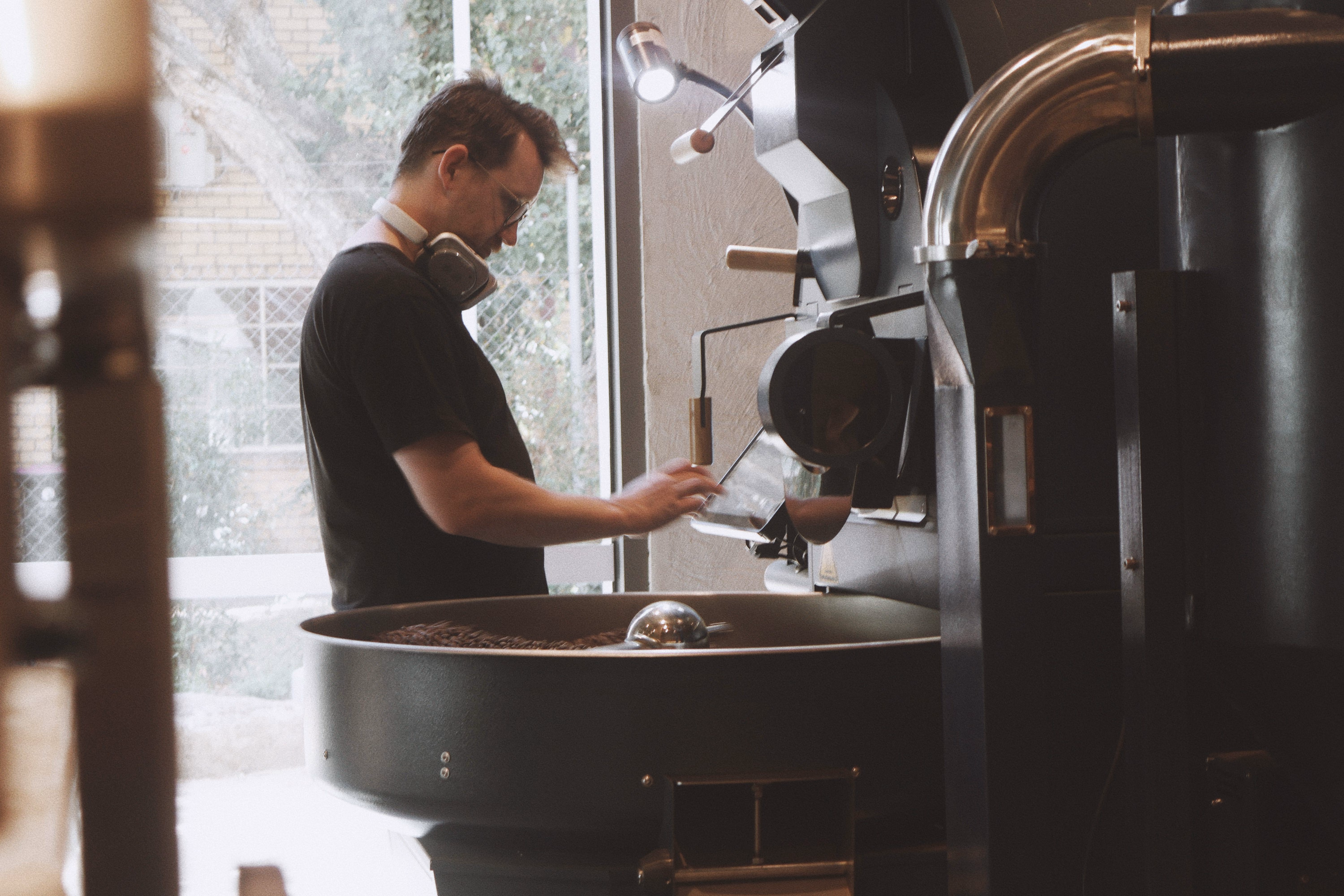 Roaster operating a drum roaster by the window in the Contraband roastery