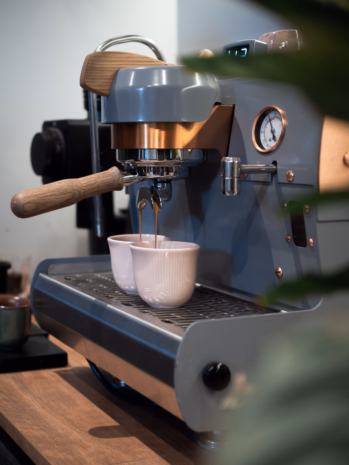 Espresso brewing into two white cups on a grey and copper espresso machine