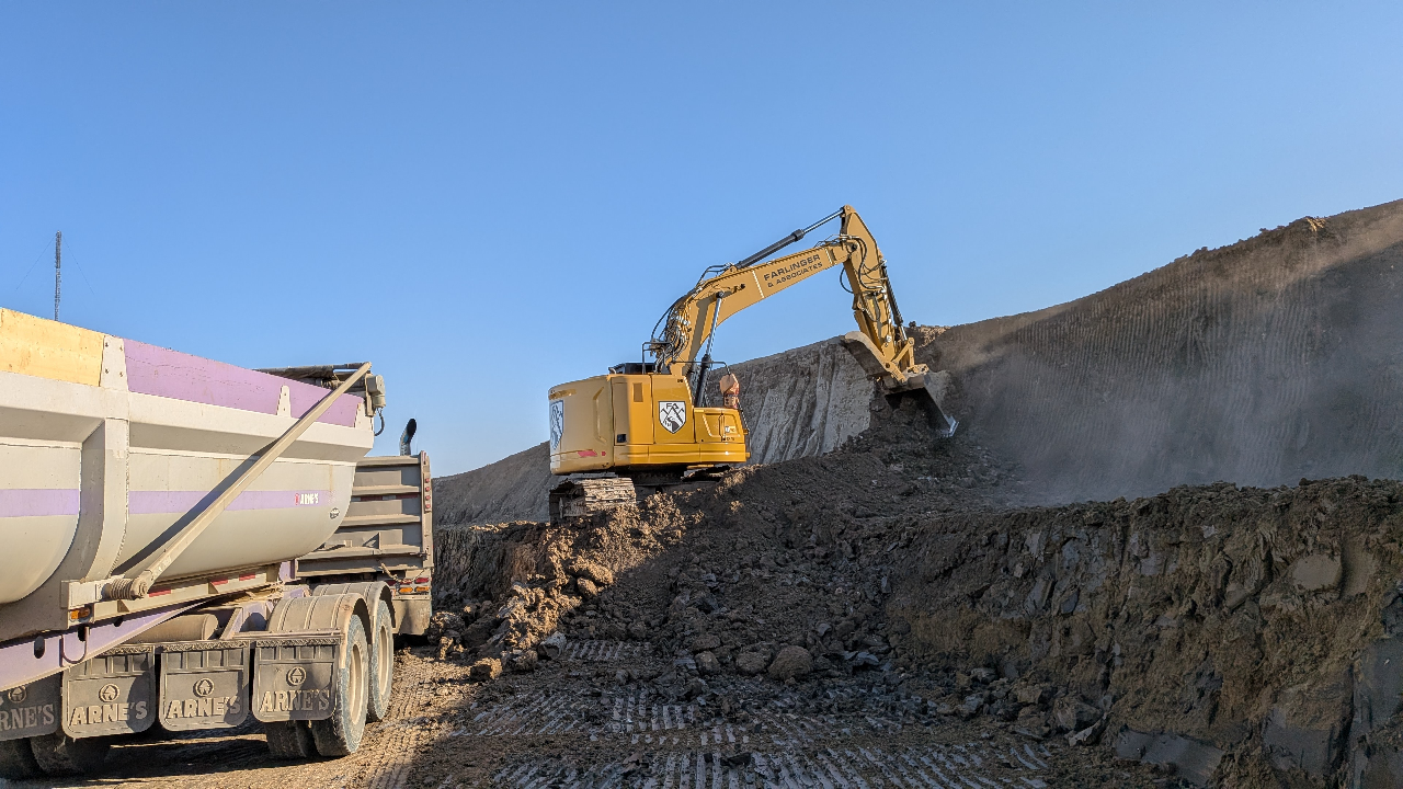 Yellow excavator loading dirt into a dump truck at a construction site under clear blue sky.