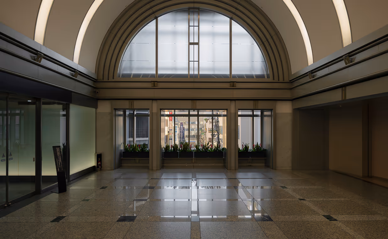 Interior space with large arched window above glass doors, tiled floor, and planters with green plants.