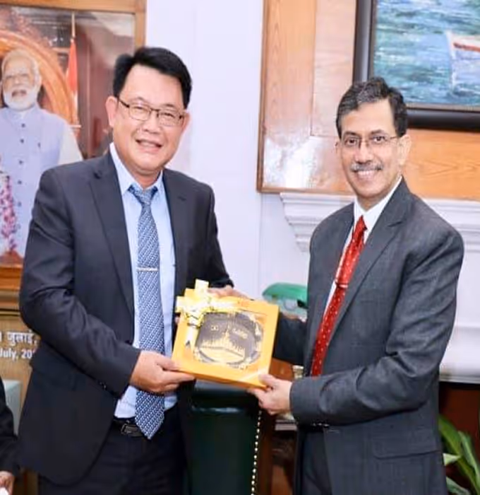 Two men in suits smiling and exchanging a gift box in an office setting.