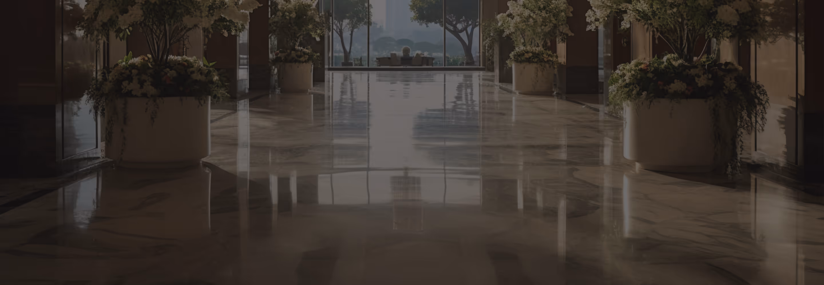 Spacious marble hallway with large flower pots and a seating area by a window overlooking trees and cityscape.