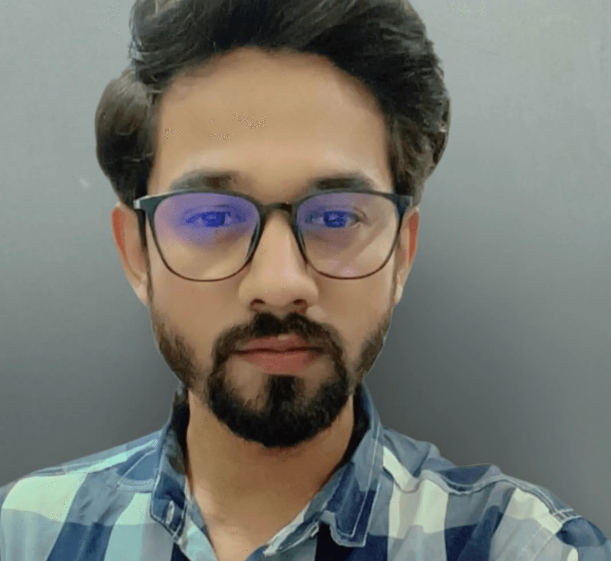 Man with beard and mustache wearing glasses and a blue and white checkered shirt against a plain gray background.