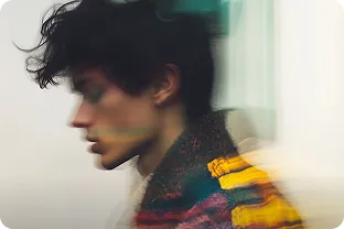 Blurred side profile of a person with curly hair wearing a colorful striped sweater.