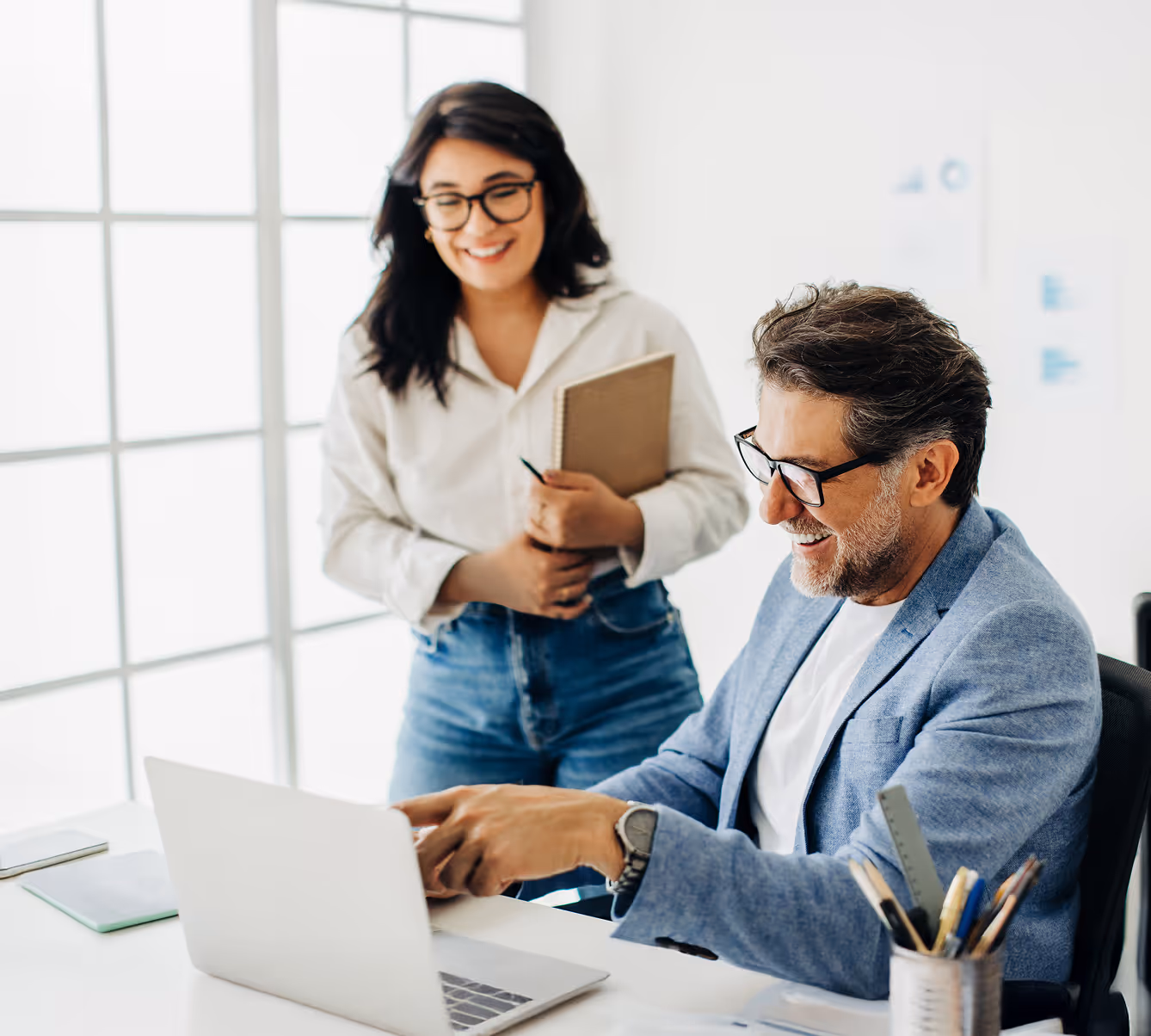 Man pointing at laptop screen and woman next to him holding notepad and pen