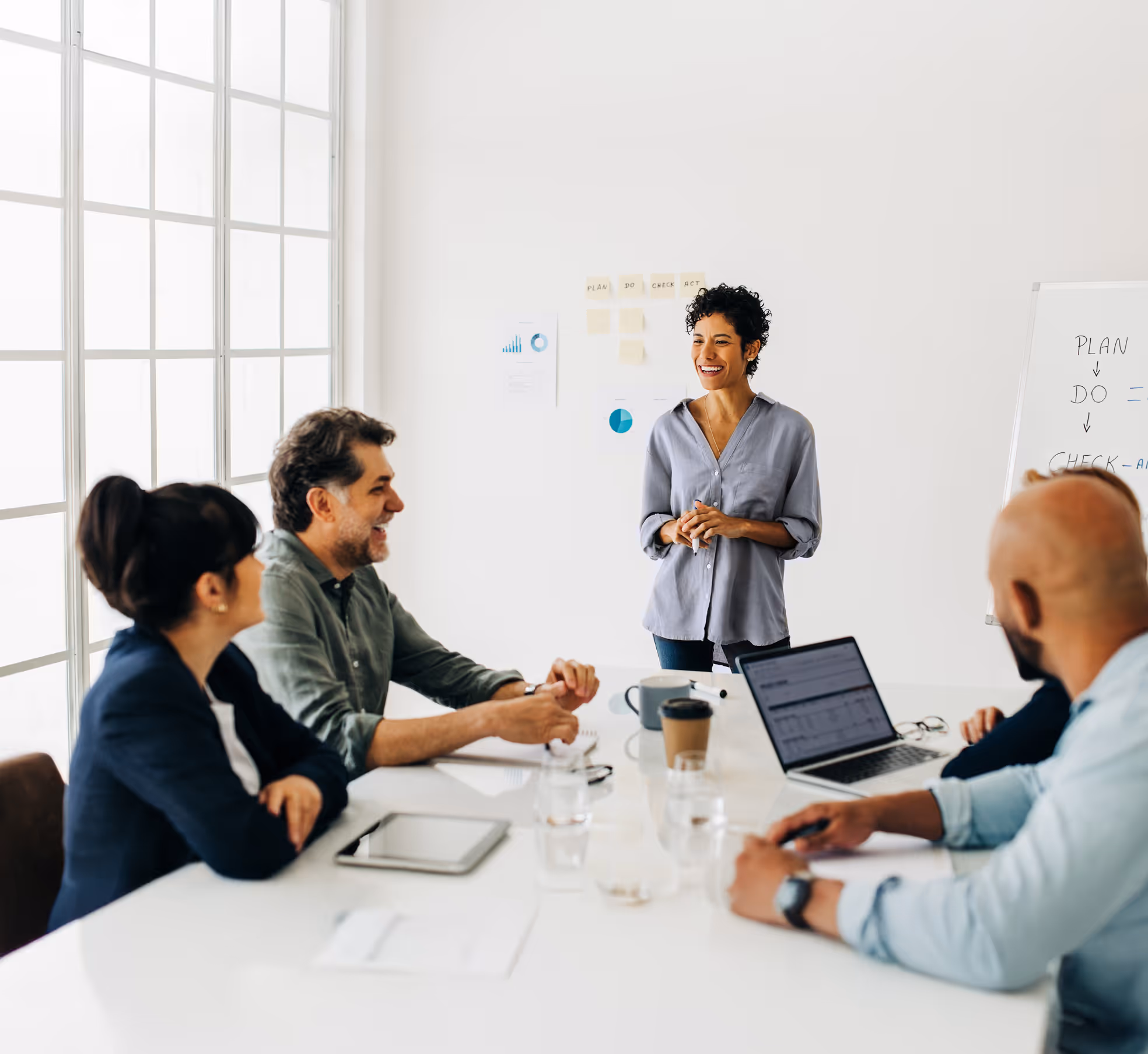 Team sitting around table with presenter standing at the front of the table looking at the team