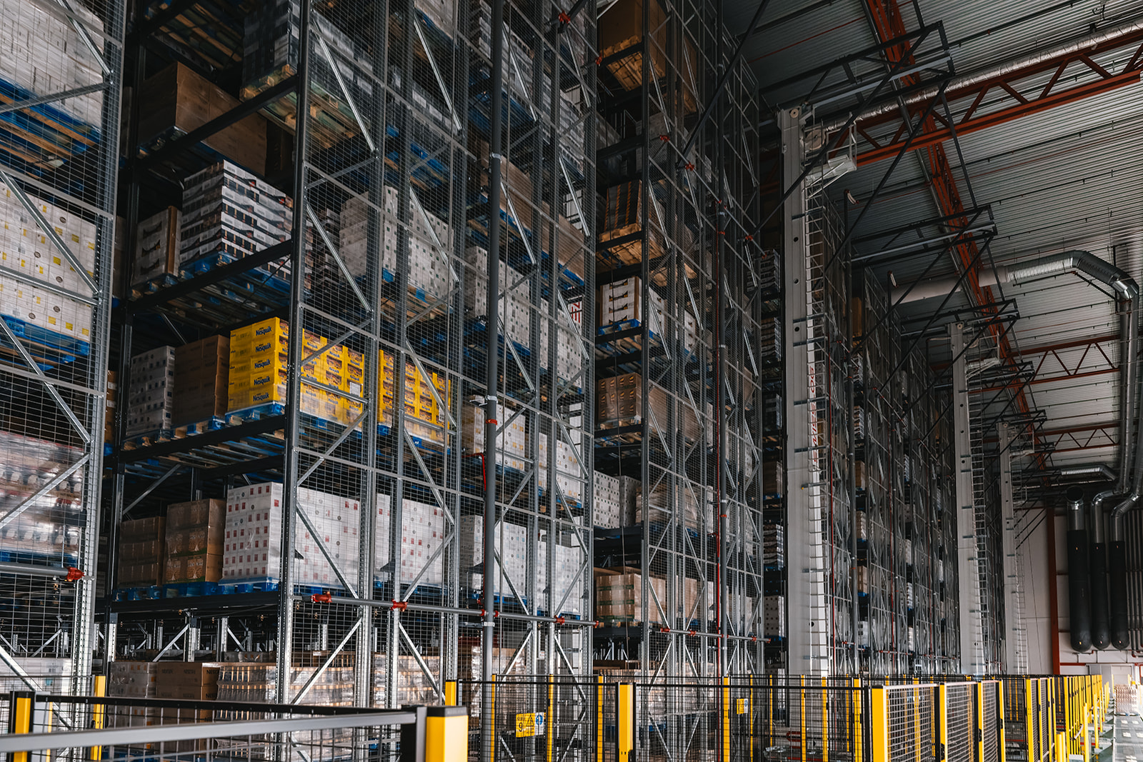 Interior of a large warehouse with tall industrial metal shelving racks filled with stacked pallets of boxed goods.