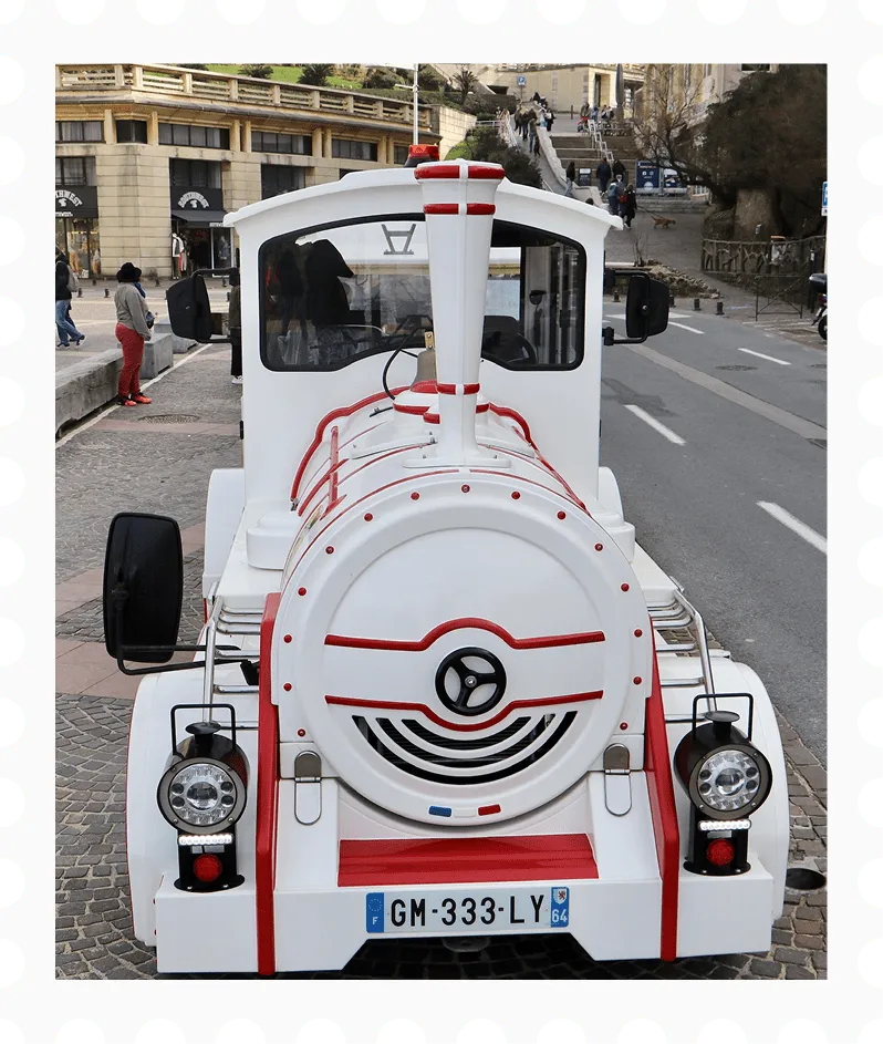 Front view of a white and red tourist train on a cobblestone street with buildings and people in the background.