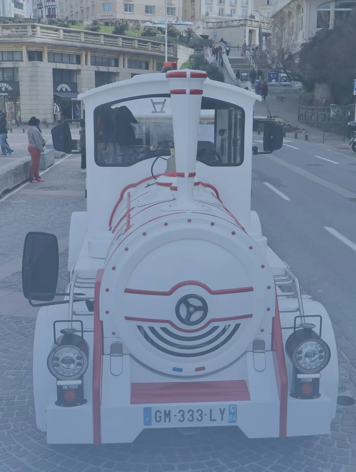 Front view of a white and red tourist train on a cobblestone street in an urban area.