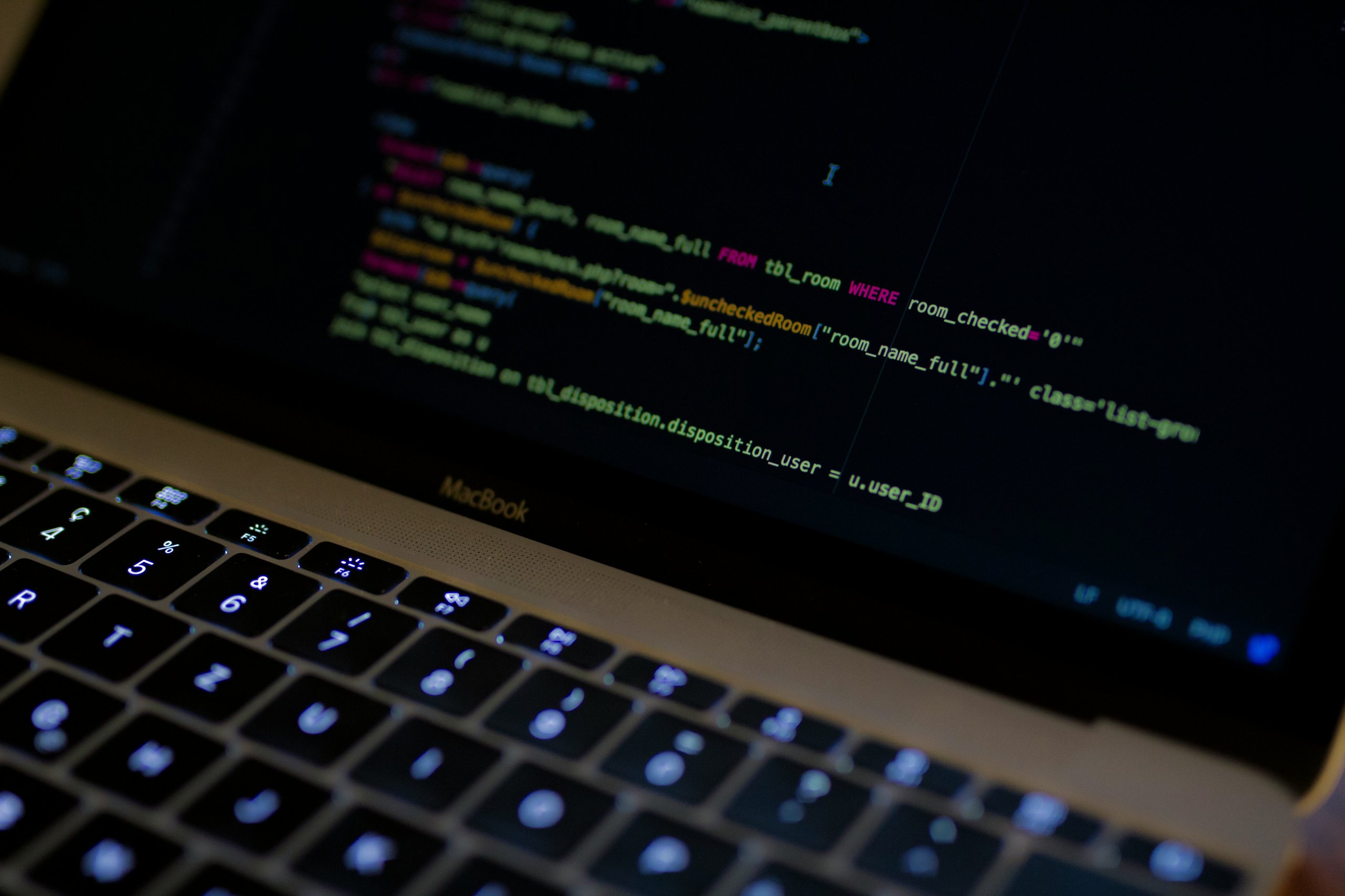 Close-up of a MacBook keyboard and screen displaying colorful lines of code.
