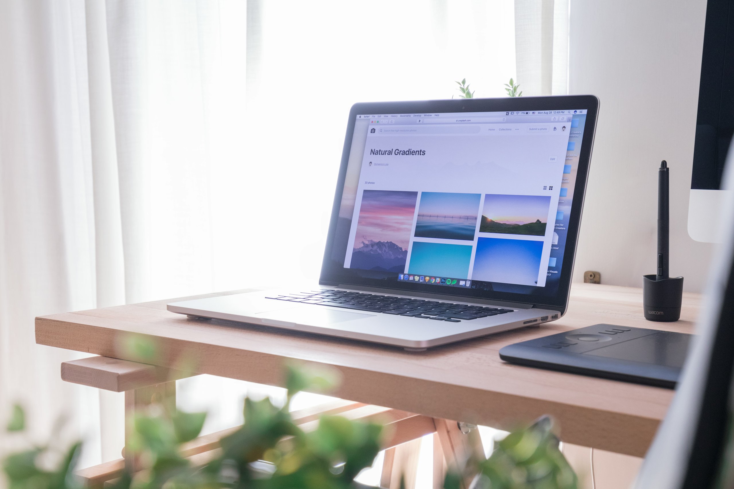 Laptop on wooden desk displaying a webpage titled Natural Gradients with landscape photos, next to a graphics tablet and pen holder.