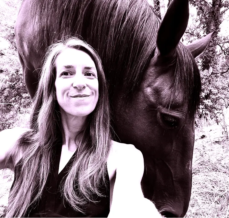 Barbara Edelmann souriante pose en selfie avec un cheval noir dont la tête est proche de la sienne en arrière-plan.