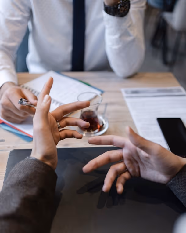 Two people having a discussion at a table with documents, a pen, tea in a glass cup, and a smartphone.