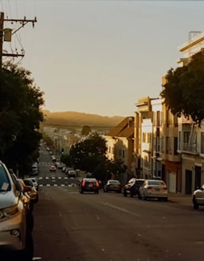Urban street lined with parked cars and buildings bathed in warm sunset light.
