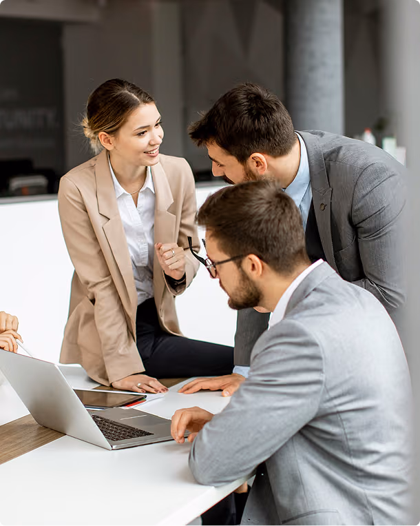 Three business professionals in suits collaborating at a table with a laptop and documents.