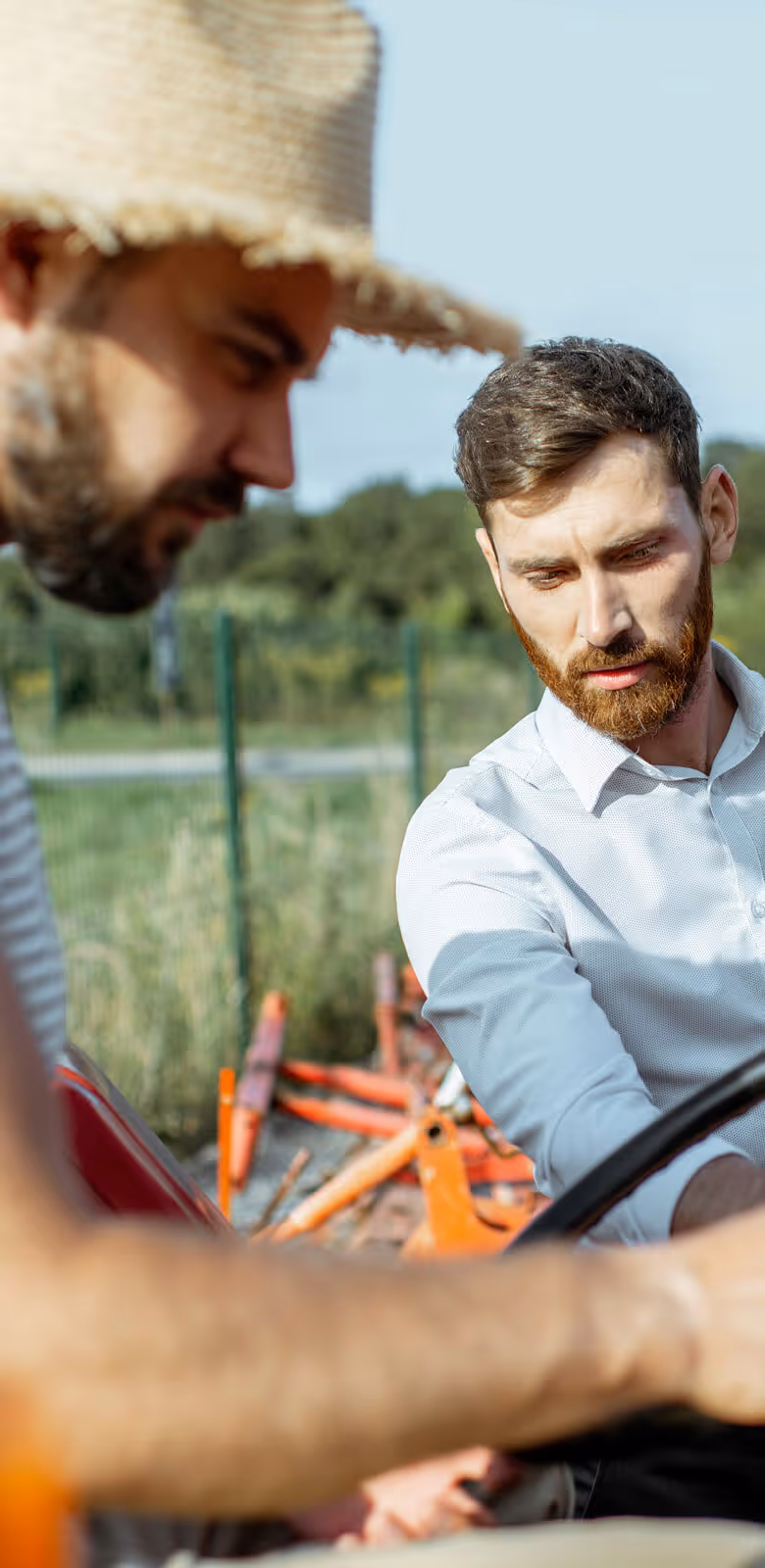 Two men examining the steering wheel of an orange tractor outside on a sunny day.