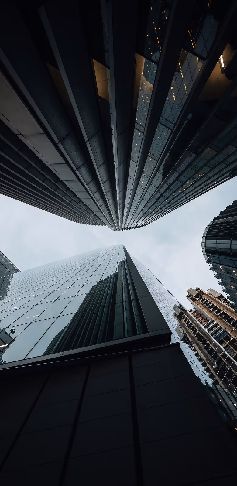 Man with beard in light blue shirt showing tractor controls to another man wearing a hat outdoors.