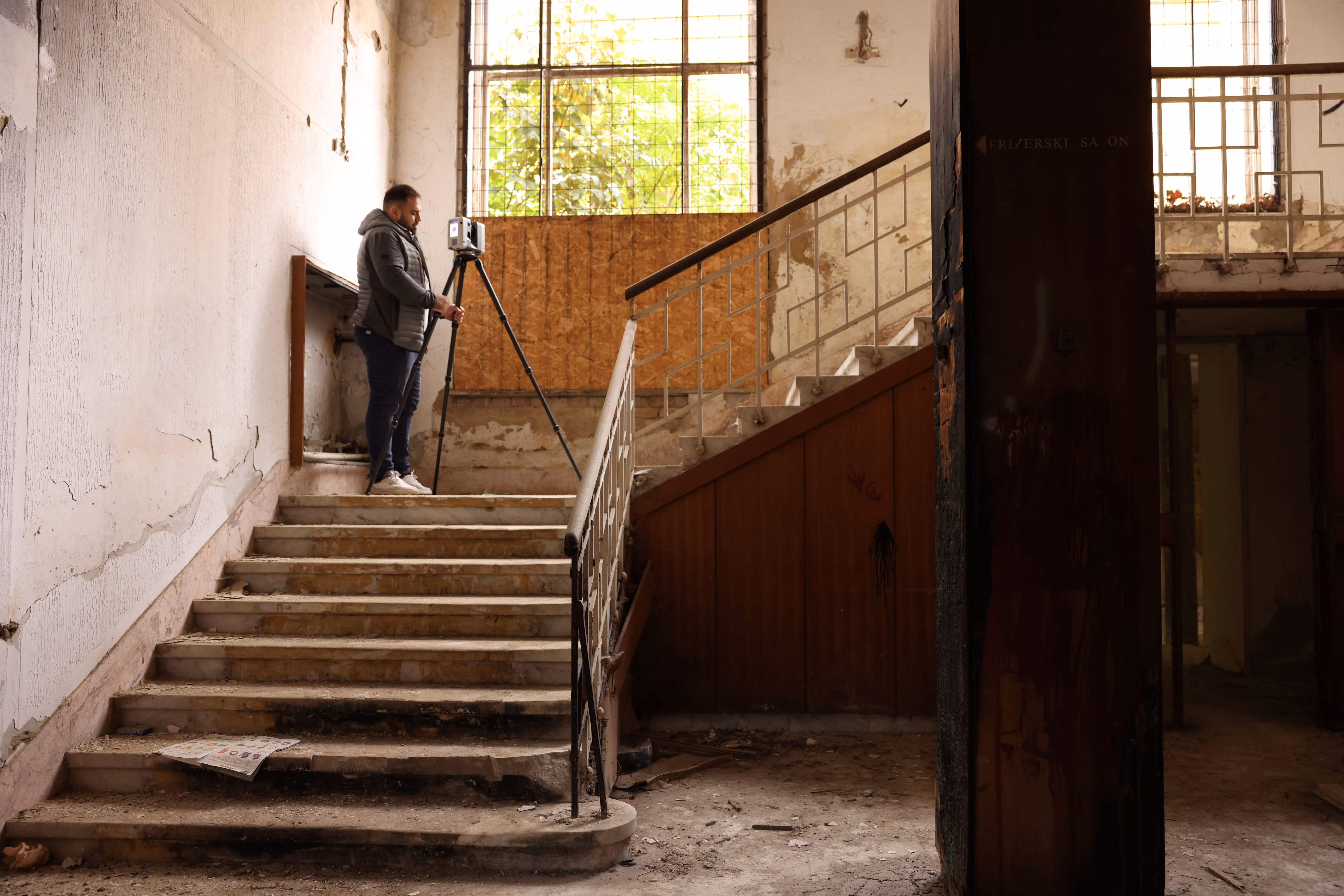 A Radin AG surveyor scanning the fire-damaged staircase of Staro Zdanje, Aranđelovac, beside a charred timber column during heritage documentation.