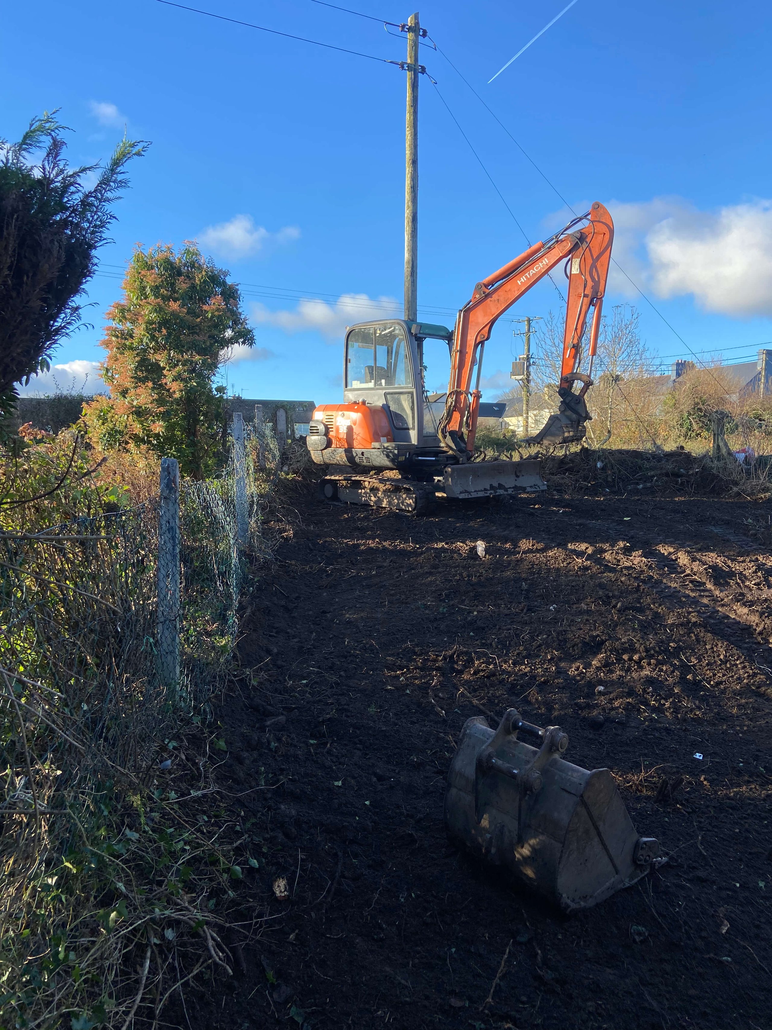 Orange Hitachi excavator on a cleared dirt construction site under blue sky with some trees and power lines.