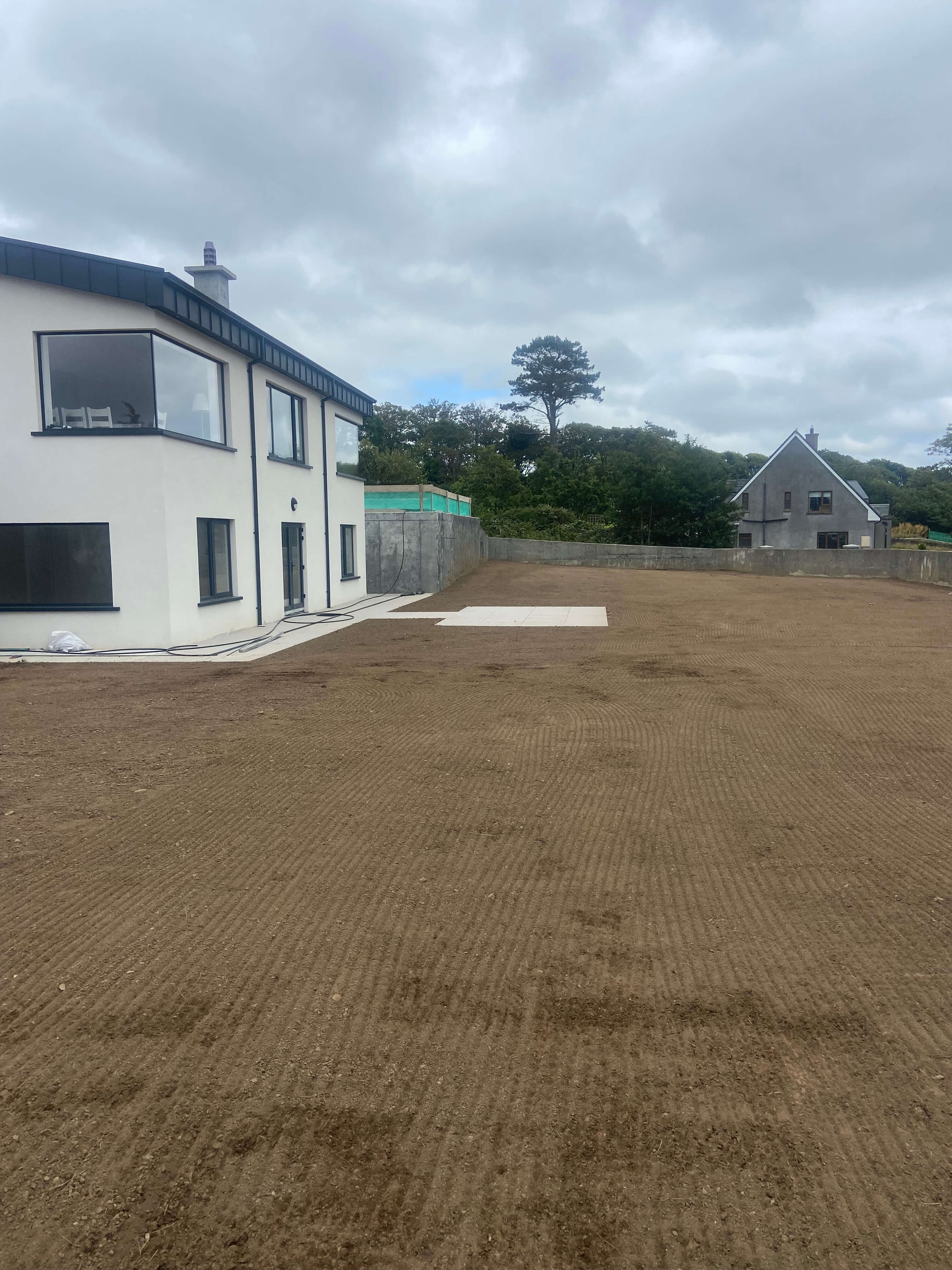 Modern white two-story house beside a large freshly tilled and leveled yard under a cloudy sky.
