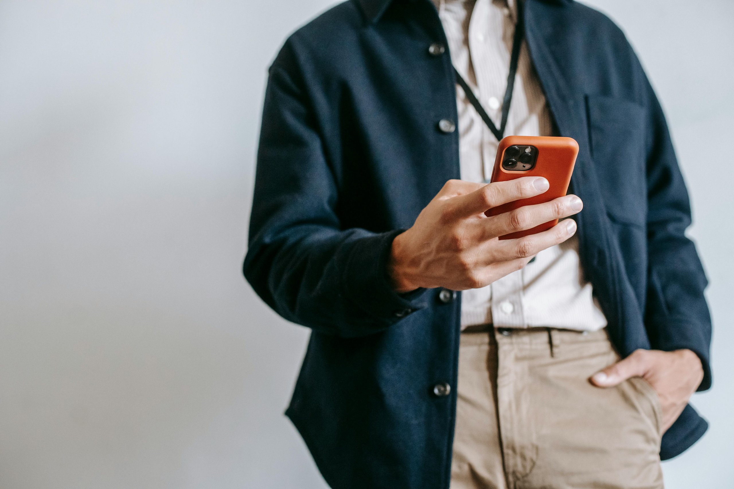 Person wearing a navy jacket and beige pants holding a smartphone with an orange case.