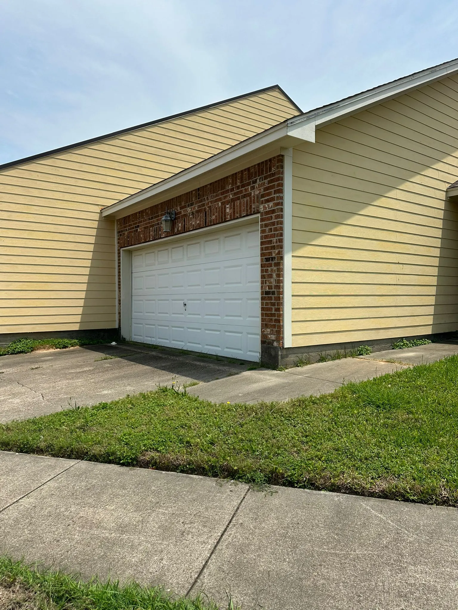Single-story garage with white door, red brick trim, and yellow siding under a partly cloudy sky.