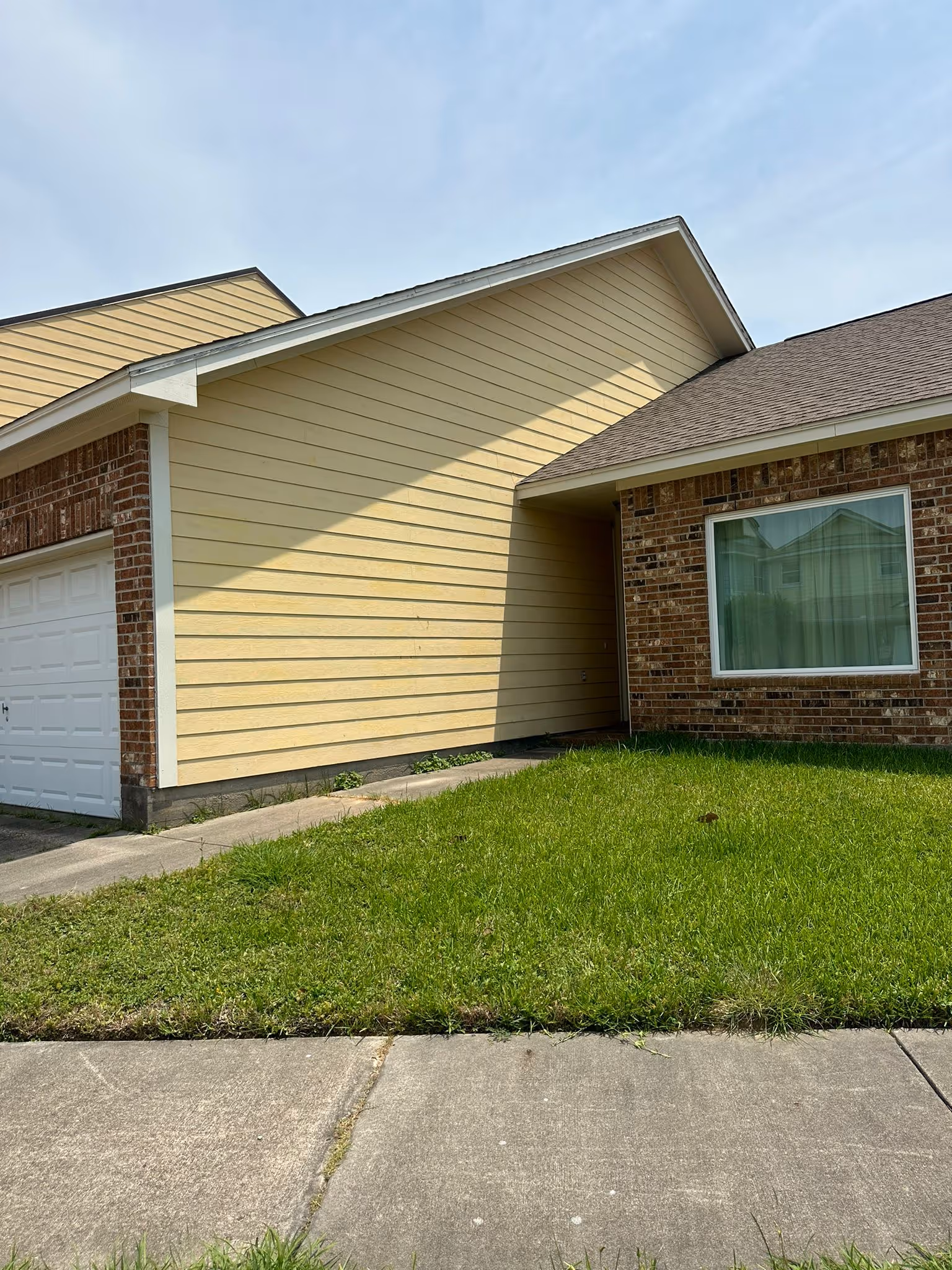 Single-story garage with white door, red brick trim, and yellow siding under a partly cloudy sky.