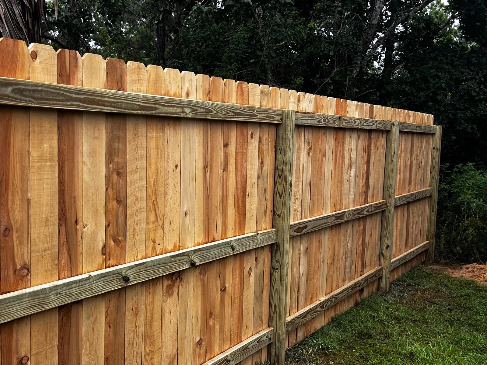 Backyard with newly installed wooden privacy fence enclosing grass, soil, and stone landscaping.