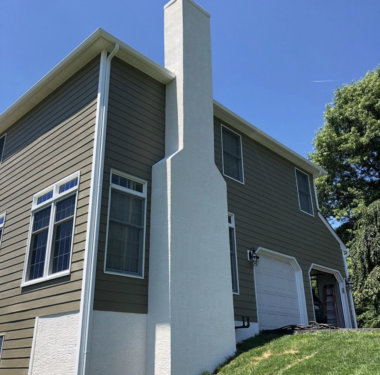 Construction site with foundation prepared with black plastic sheeting and metal rebar grid, small excavators and trees in the background.