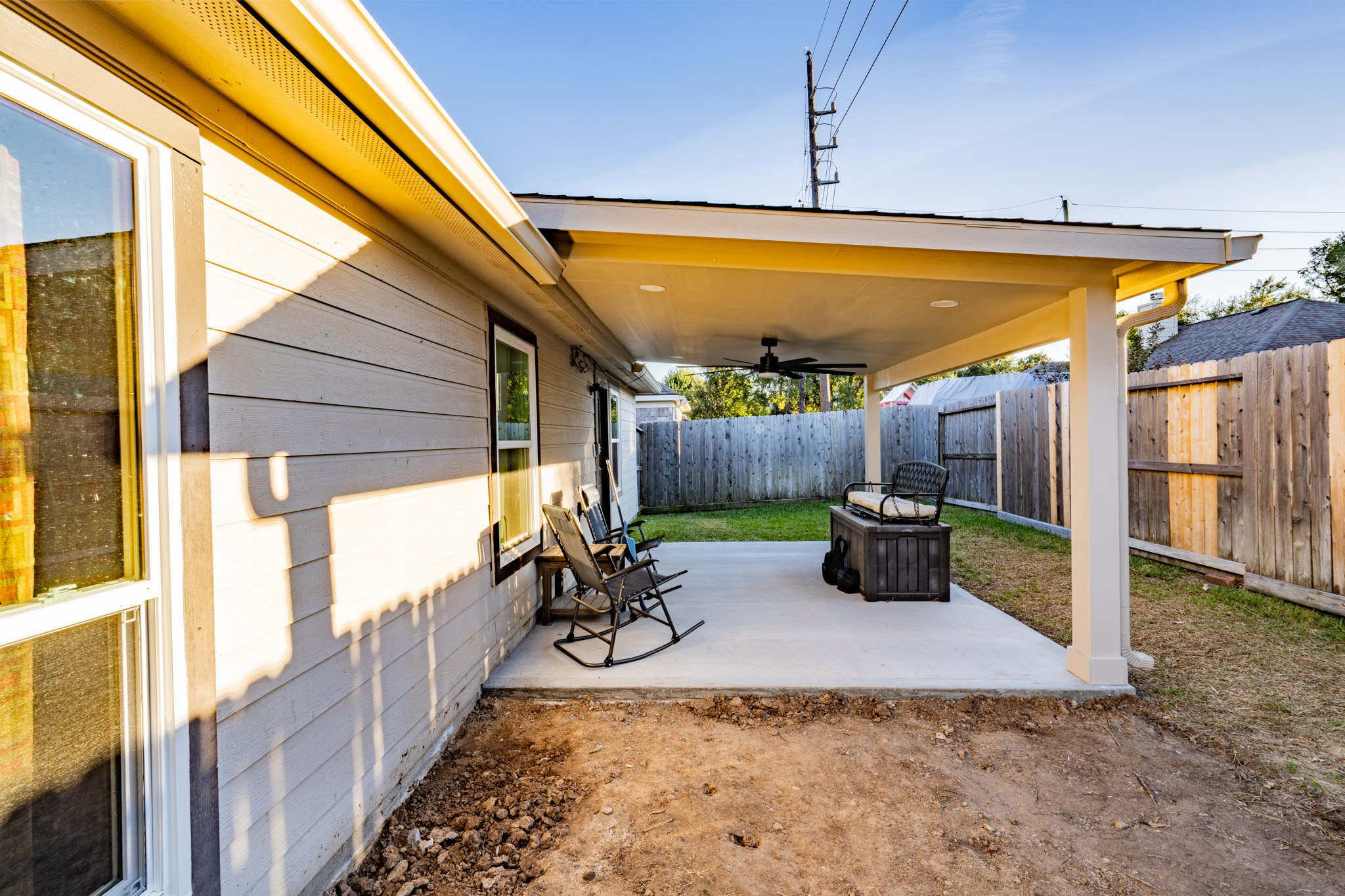 Construction site with foundation prepared with black plastic sheeting and metal rebar grid, small excavators and trees in the background.