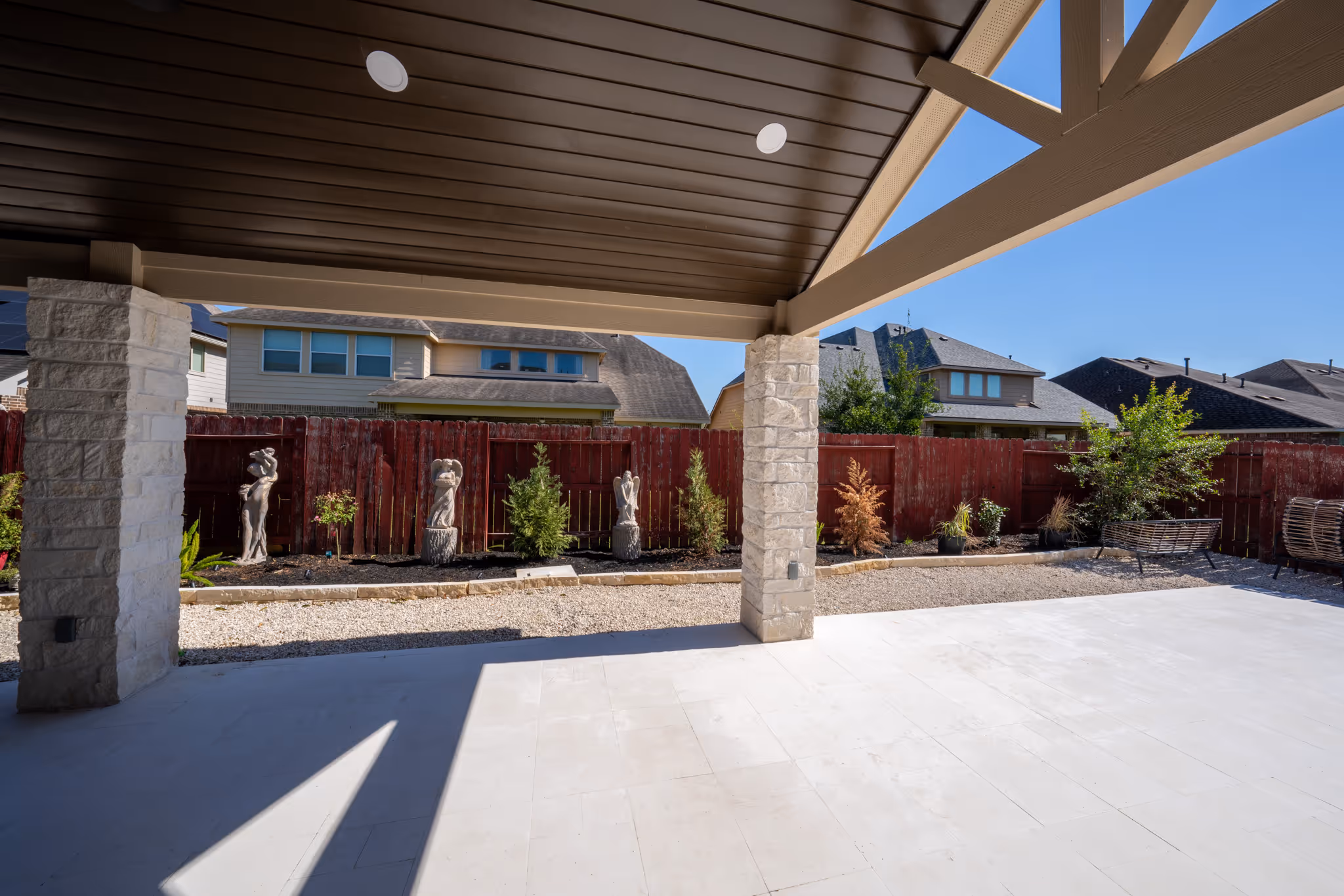 Covered patio with stone-clad columns, a dark stained ceiling with recessed lights and a new light concrete slab.