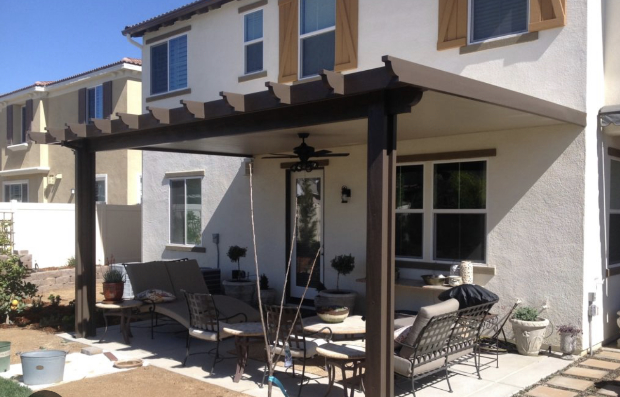 Covered patio with a ceiling fan and outdoor seating behind a two-story home.