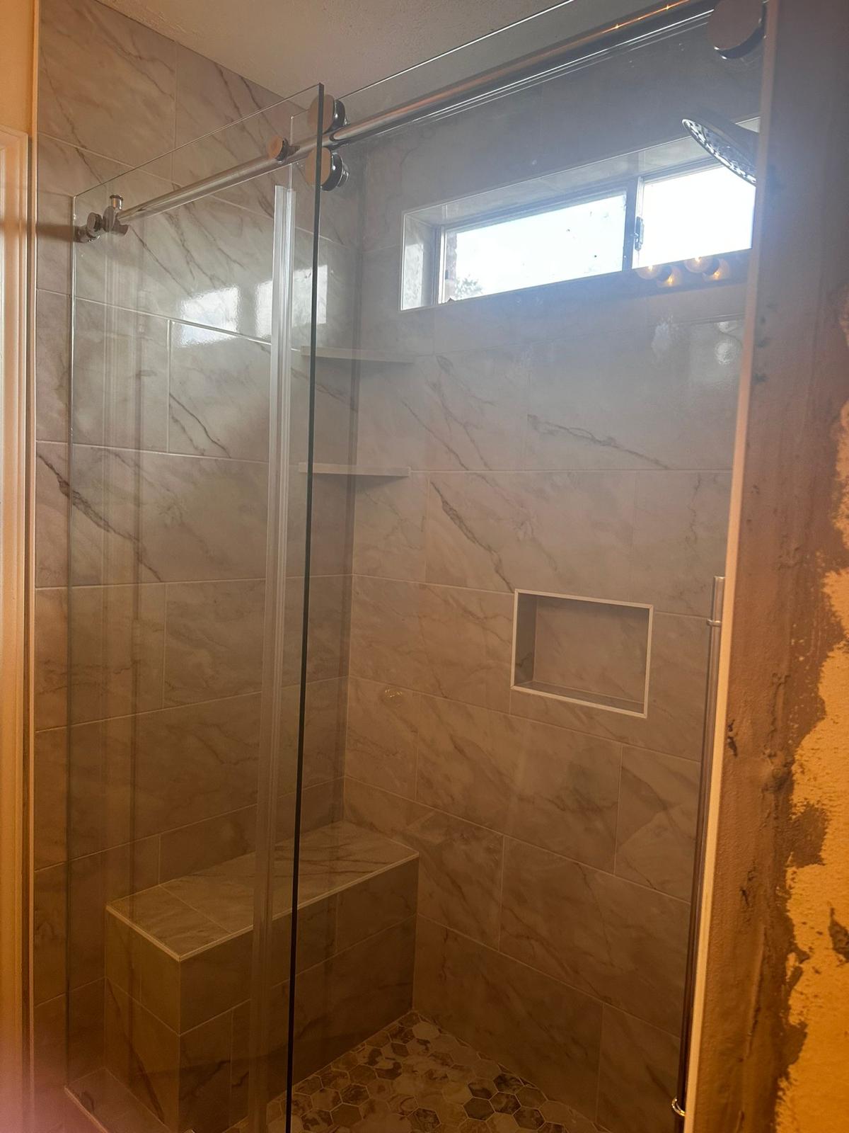 Shower with warm brown large-format tile, a built-in bench, a recessed niche, and a sliding glass door.