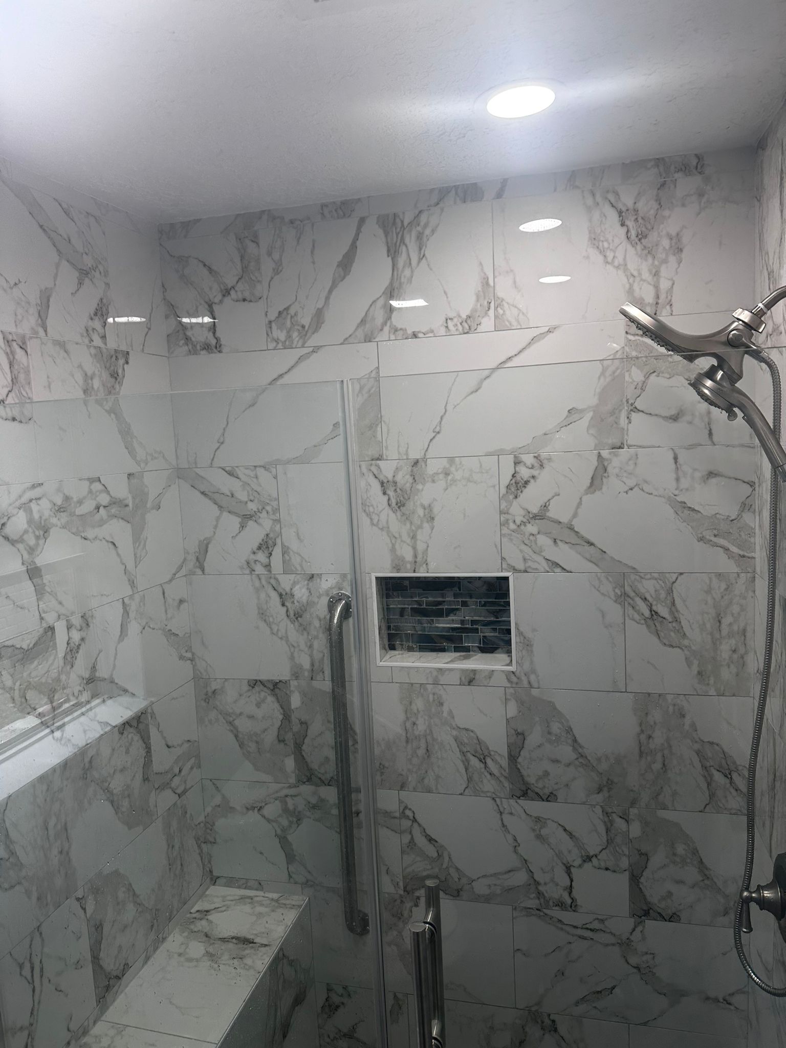 Walk-in shower with floor-to-ceiling marble-look porcelain tile, a recessed niche, a grab bar, and a handheld shower head.