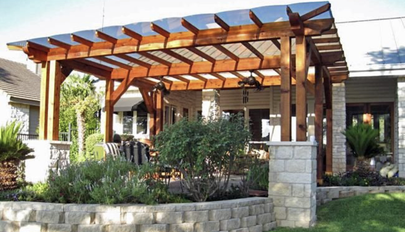 Cedar pergola over a stone-edged patio with landscaped beds behind a brick home.