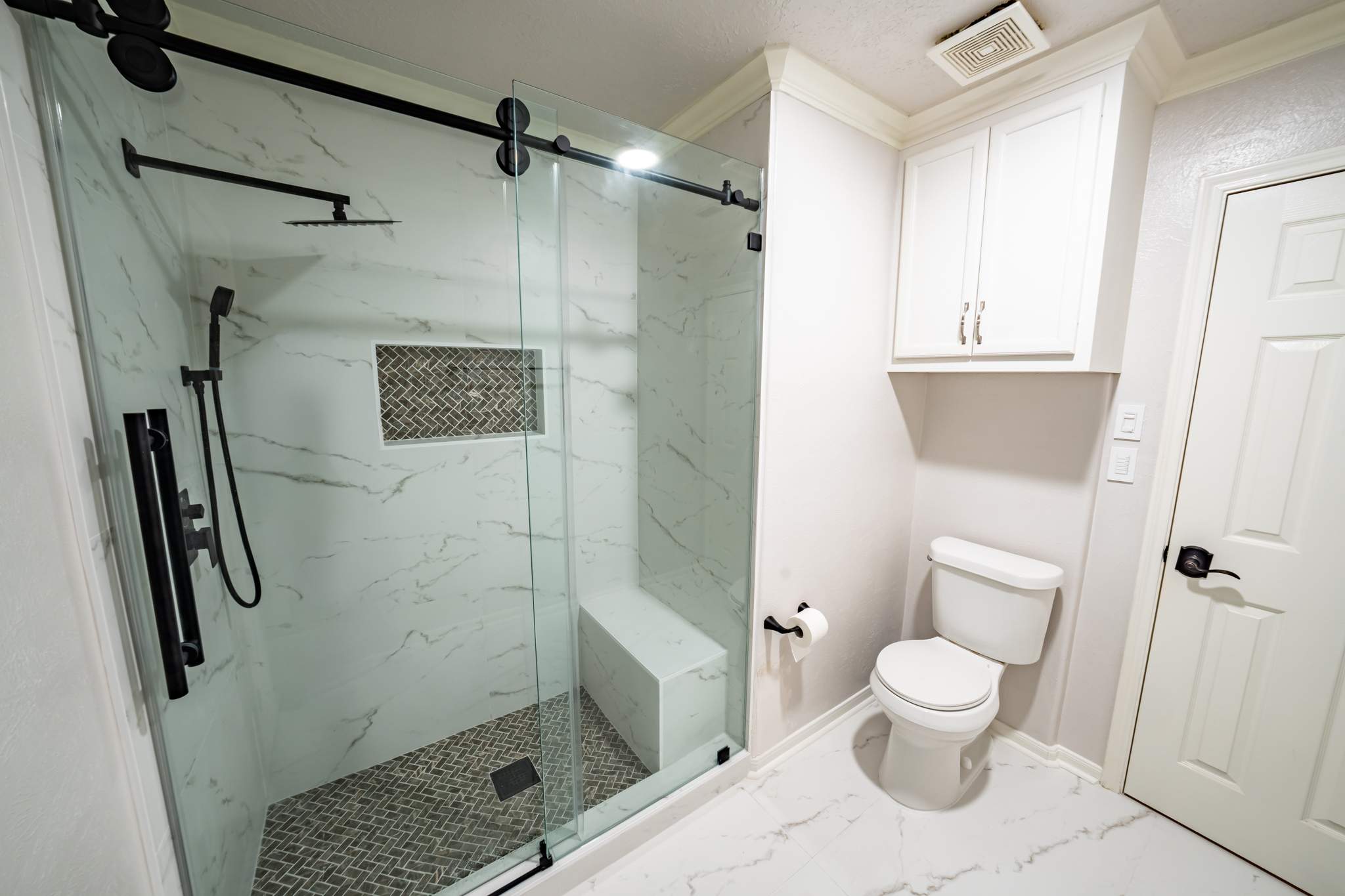 Remodeled Houston bathroom with a frameless glass walk-in shower, marble-look tile, a built-in bench, and a mosaic shower floor.