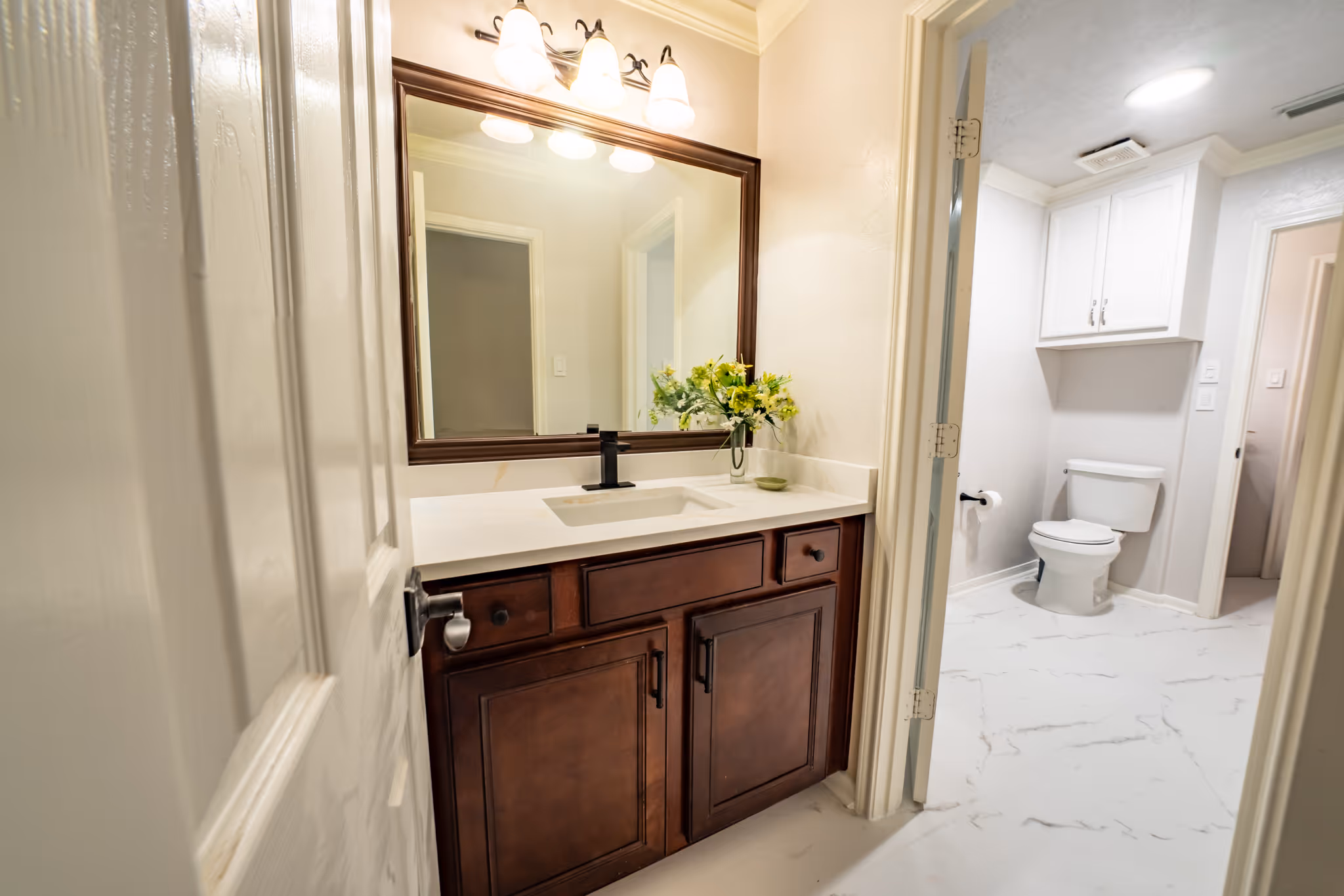 Bathroom with a dark wood vanity, a framed mirror, marble-look floor tile, and a separate toilet area.